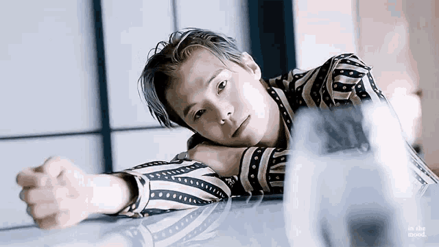 a young man in a striped shirt is laying on a table with his head on his arm .