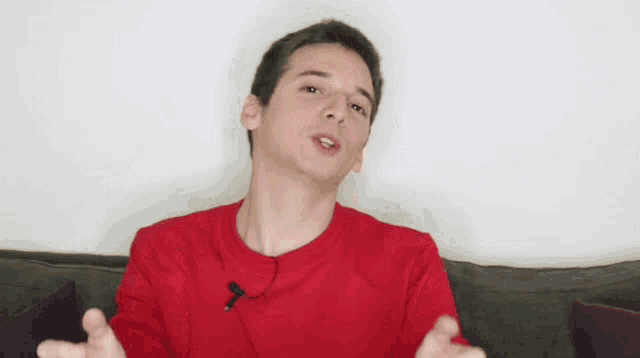 a young man in a red shirt is making a funny face with his eyes closed