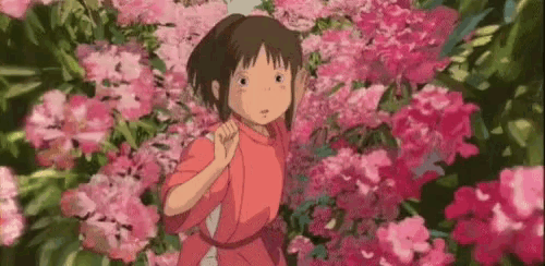 a girl in a red shirt is standing in a garden of pink flowers .