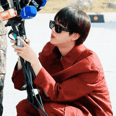 a man wearing sunglasses is kneeling down holding a microphone with kbs written on it