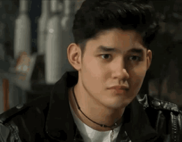 a young man wearing a black leather jacket and a choker is looking at the camera .