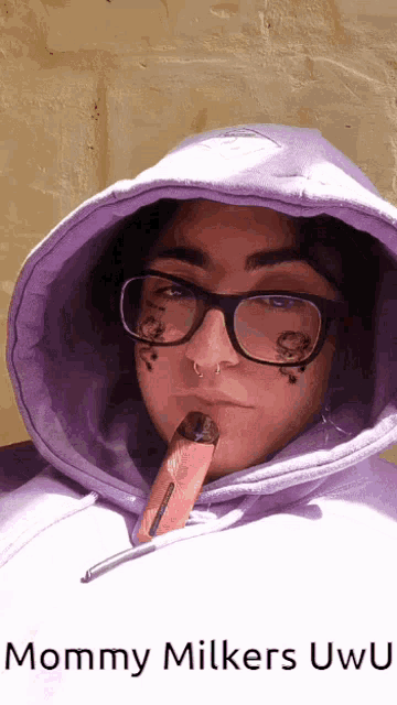 a woman wearing glasses and a purple hoodie is smoking an electronic cigarette and says mommy milkers uwu on the bottom