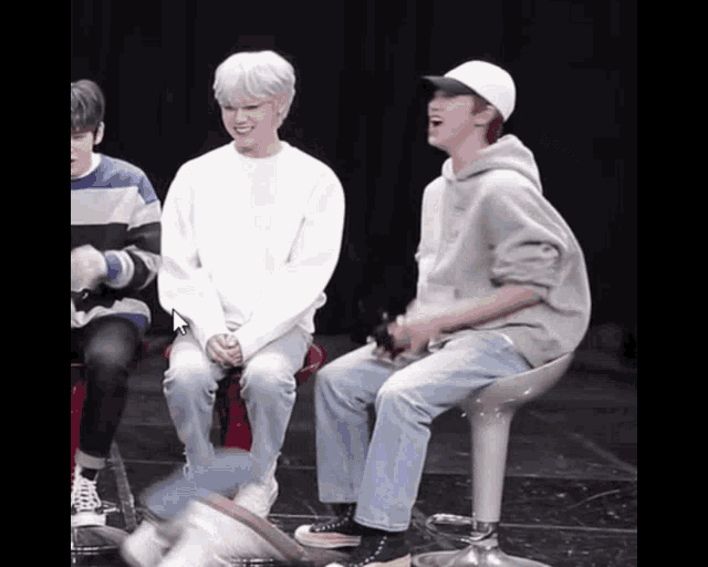 a group of young men are sitting on stools and one of them is wearing a white hat