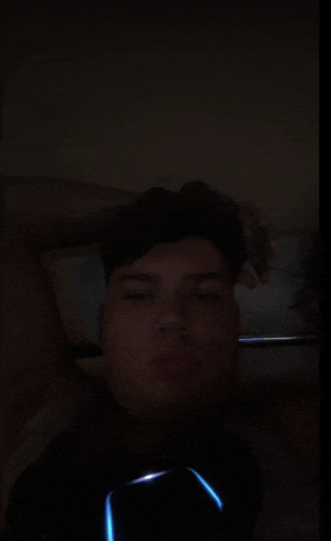 a young man is laying on a bed with his eyes closed and holding a cell phone .