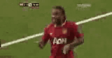 a soccer player wearing a red aon jersey is running on the field .