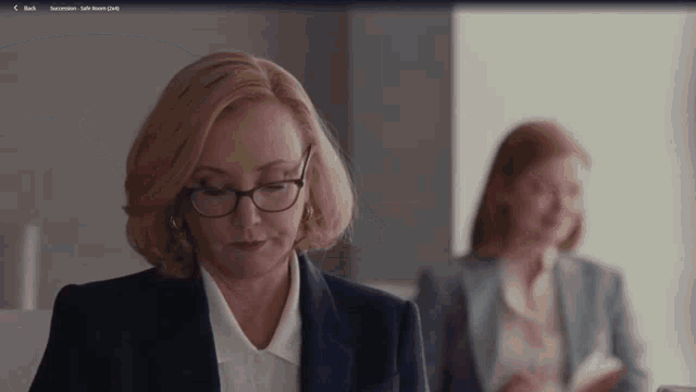 a woman wearing glasses and a suit is sitting in front of another woman