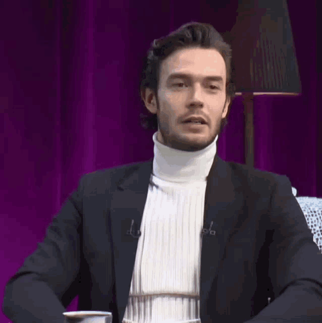 a man wearing a white turtleneck and a black jacket with the letter a on the collar
