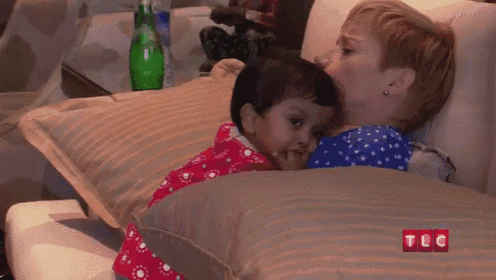 a woman is laying on a couch with a baby on her lap and the words tlc on the bottom right corner .