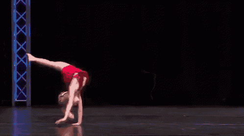 a woman in a red dress is doing a handstand on a black stage .