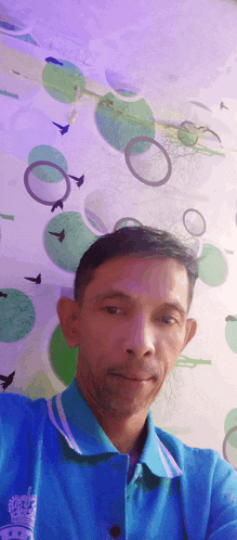 a man in a blue shirt is taking a selfie in front of a wall with circles on it