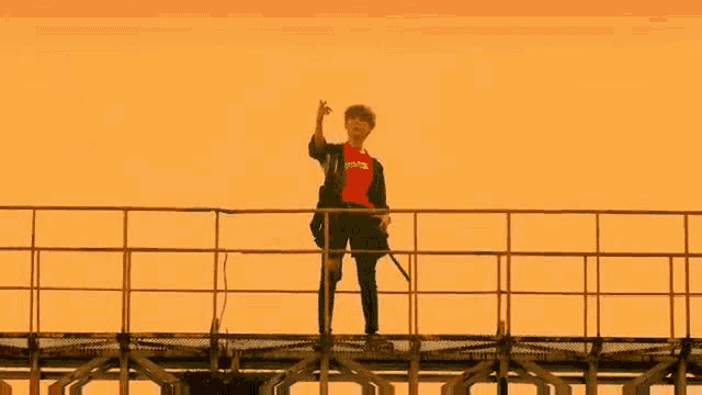 a man in a red shirt is standing on top of a bridge .