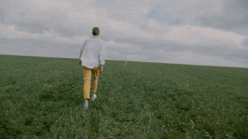 a man in a white shirt and yellow pants walking through a grassy field