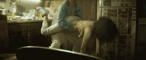 a person is laying on another person 's back in a kitchen