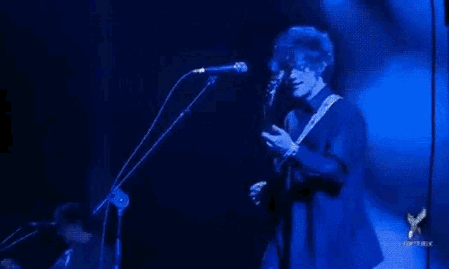 a man is singing into a microphone while playing a guitar on a stage .