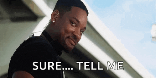 a man wearing a bullet proof vest is standing in front of a bridge and says `` sure ... tell me '' .