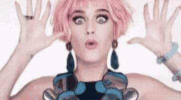 a woman with pink hair and a blue necklace is making a funny face with her hands .