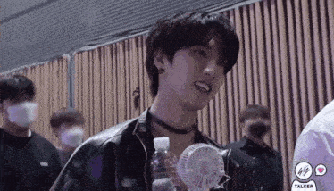 a young man is holding a small fan and a bottle of water in front of a wooden wall .