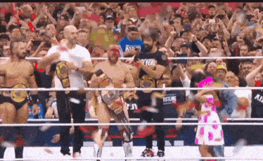 a group of wrestlers are standing in a ring with a crowd behind them .