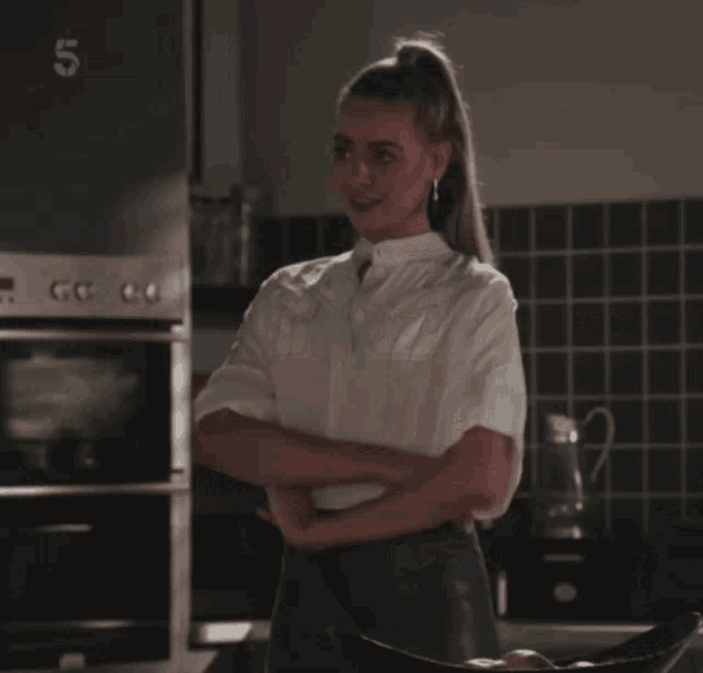 a woman in a white shirt is standing in front of a stove with the number 5 on it