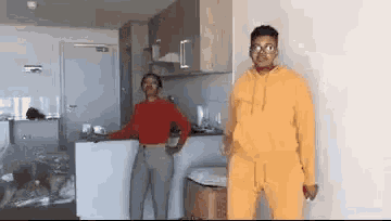 a man in a yellow hoodie is standing next to a woman in a red top in a kitchen .