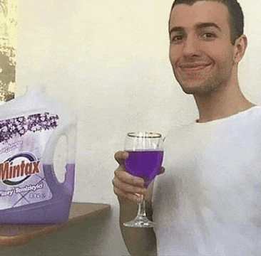 a man is holding a glass of purple wine in front of a bottle of mintox lavender .