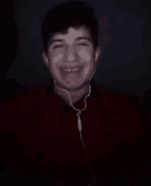 a young man wearing ear buds is smiling in the dark