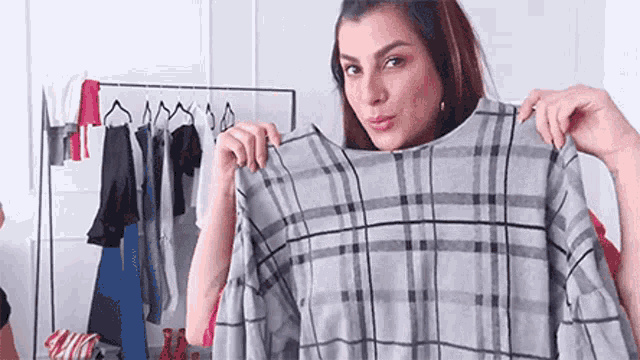 a woman is holding a plaid sweater in front of a clothes rack .