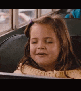a little girl is sitting on a bus with her eyes closed and making a funny face .