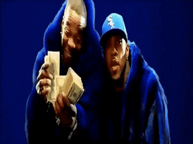a man in a blue fur coat is holding a bunch of money next to another man in a blue hat .