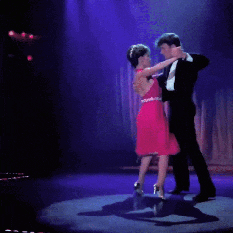 a woman in a pink dress is dancing with a man in a suit on a stage