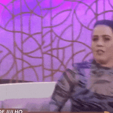 a woman is sitting on a couch with her arms outstretched in front of a purple background .