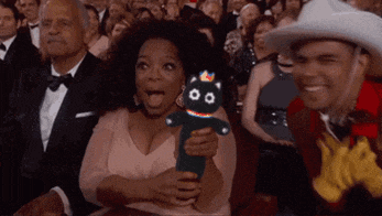 a woman is holding a stuffed animal with a crown on it in front of a crowd