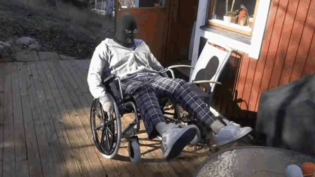 a man wearing a mask sits in a wheelchair on a deck