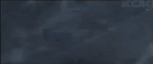 a close up of a person holding a gun in a dark room with smoke coming out of it .