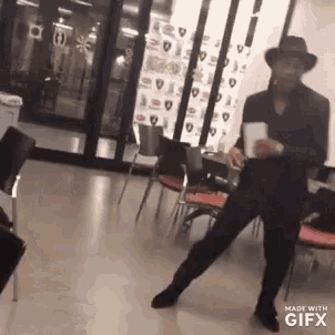 a man in a cowboy hat is dancing in a room with chairs and tables .