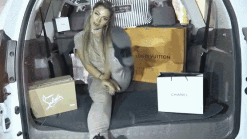 a woman sits in the back of a car surrounded by louis vuitton bags and boxes