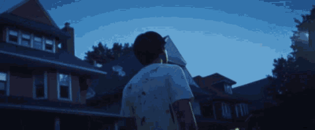 a man with blood on his shirt stands in front of houses