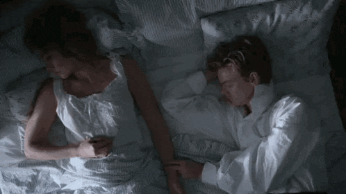 a man and a woman are sleeping next to each other in bed holding hands .