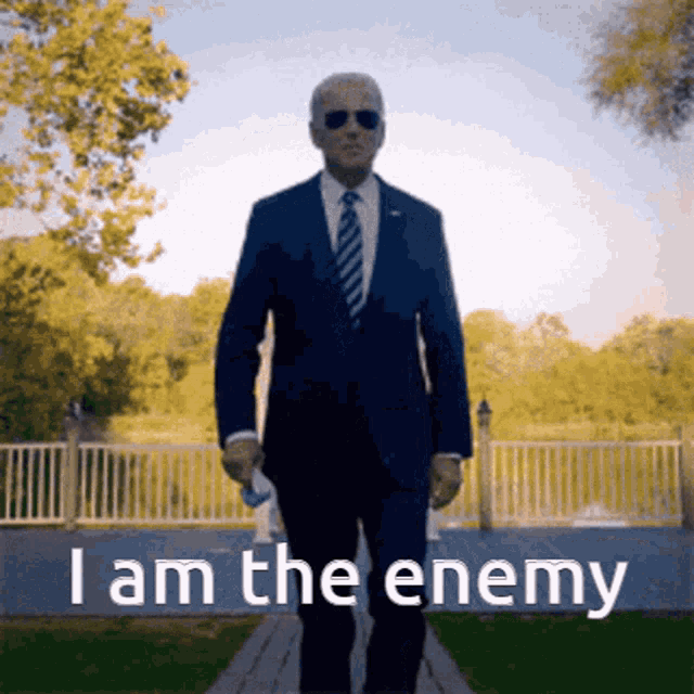 a man in a suit and tie is walking down a path with the words " i am the enemy " on the bottom