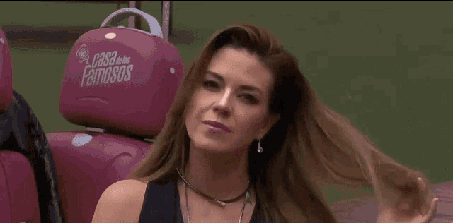 a woman adjusts her hair in front of a car seat that says casa dos famosos on it