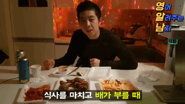 a man sitting at a table with plates of food and a can of soda