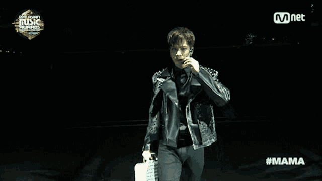 a man in a leather jacket stands in front of a screen that says mnet