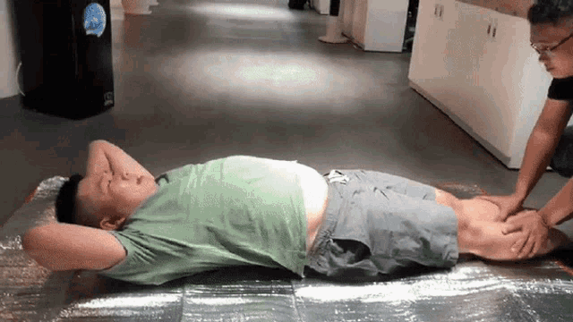 a man in a green shirt is laying on the floor while another man massages his legs