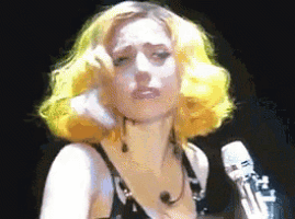 a woman with yellow hair is singing into a microphone on stage