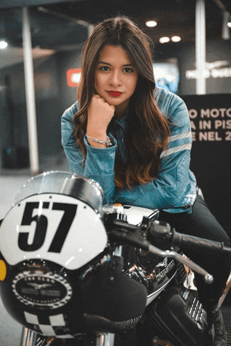 a woman is sitting on a motorcycle with the number 57 on the front