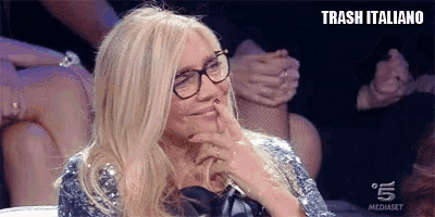 a woman wearing glasses and a sequined top is sitting in front of a group of people .