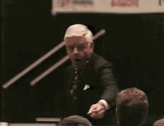 a man in a suit and tie stands in front of a microphone with the word whoop behind him
