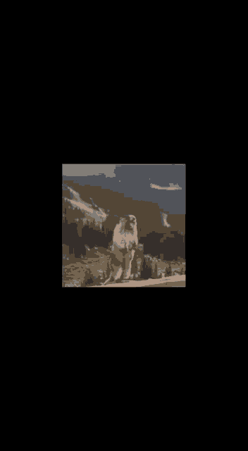 a ground squirrel is standing on its hind legs in front of a mountain range .