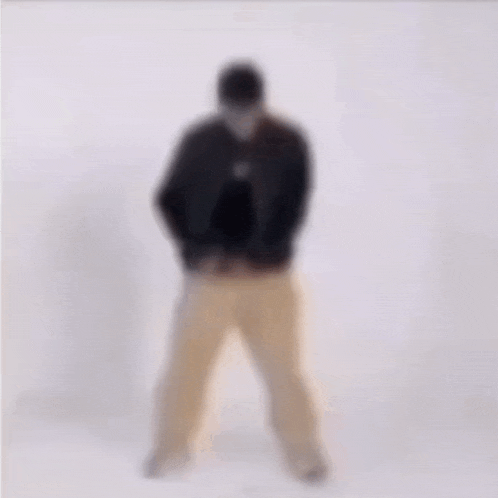 a blurry picture of a man in a black jacket and tan pants standing on a white background .