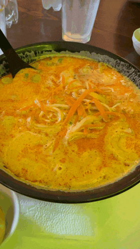 a bowl of soup with noodles and carrots on a table